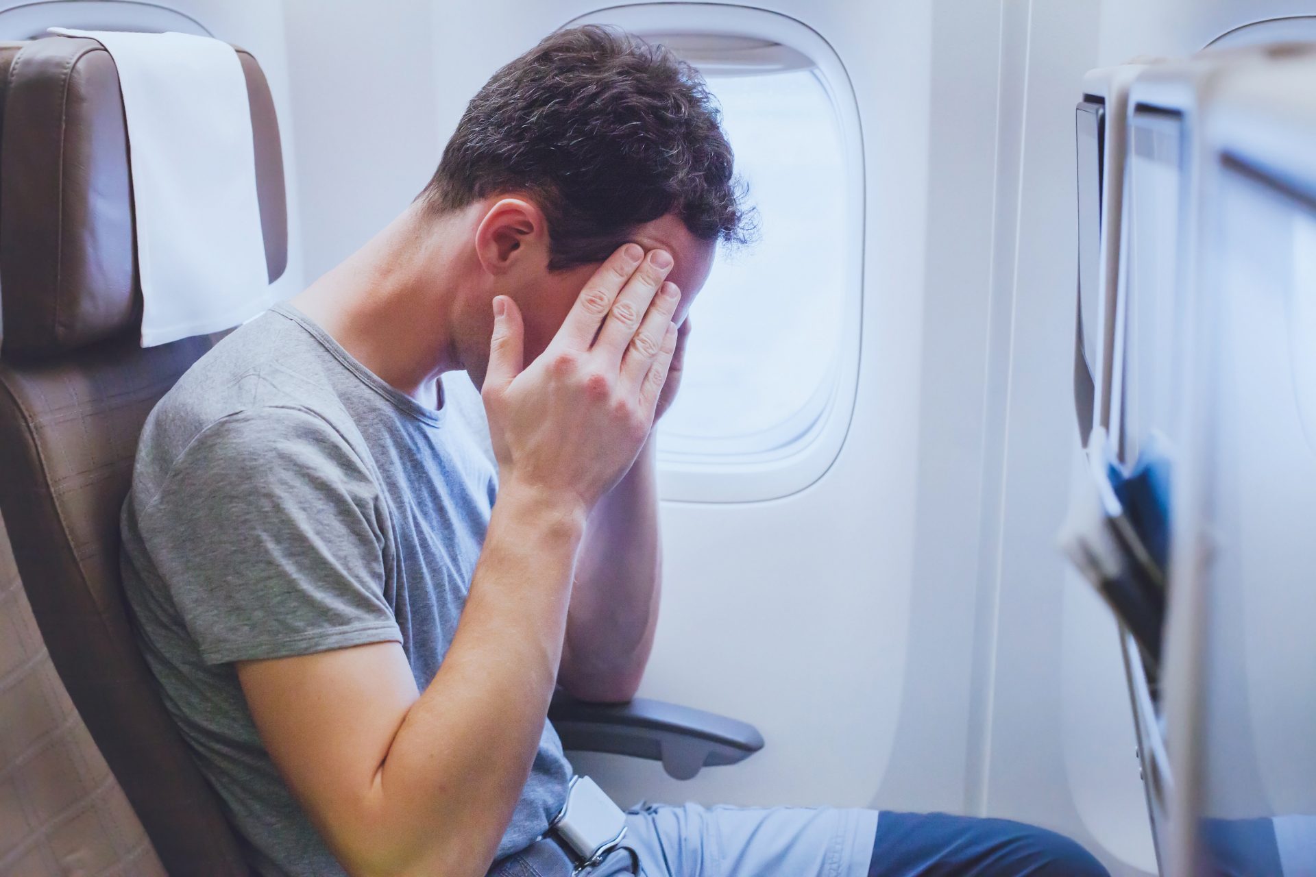 Man experiencing discomfort on a flight, touching his forehead