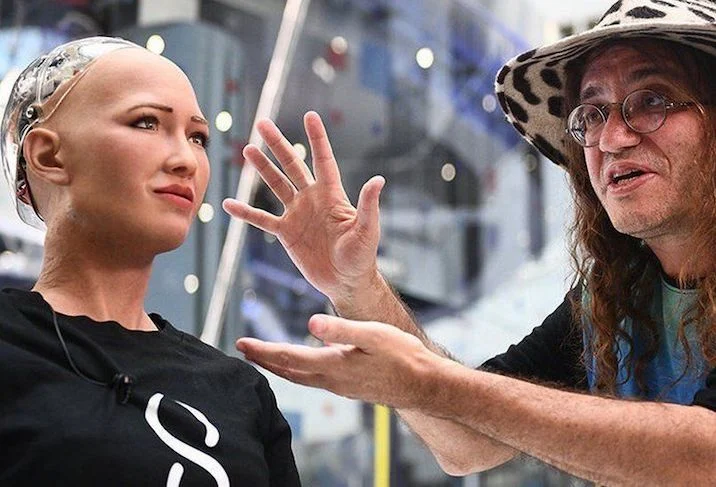 Ben Goertzel standing beside Sophia, the humanoid robot, discussing AI advancements.